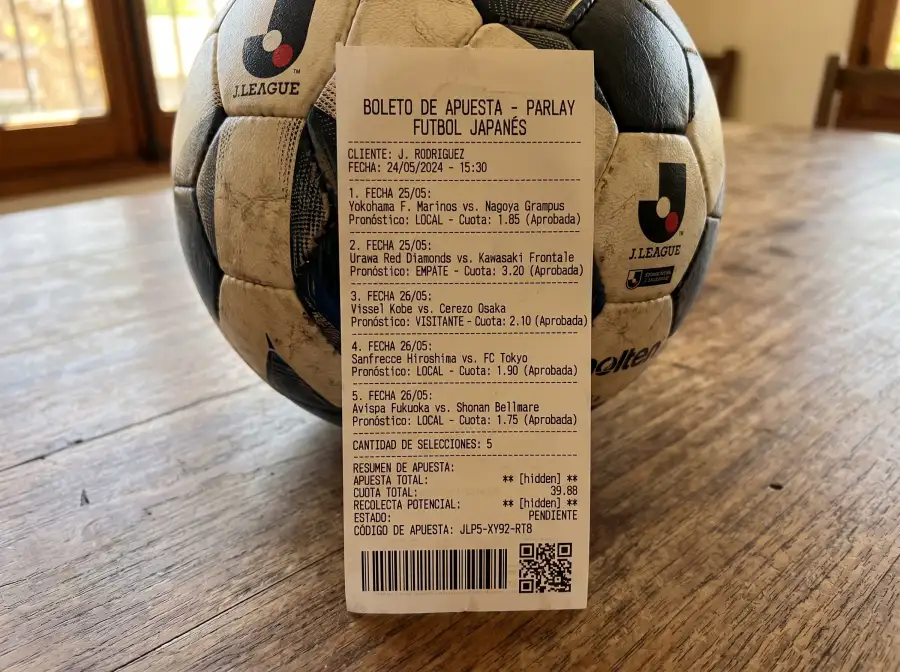 Boleto impreso de apuesta combinada con varios partidos de J League marcados junto a un balón de fútbol